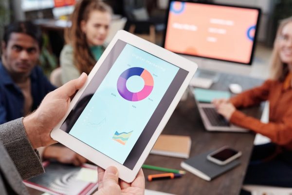 Business team using a tablet to analyze digital marketing data with charts in an office setting.