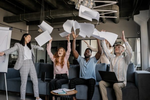 Diverse coworkers celebrate success by throwing papers in modern office setting.
